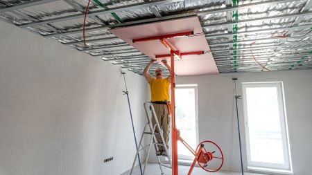 Pracownik instalujący płytę sufitową za pomocą podnośnika do montażu płyt k-g